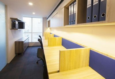 Narrow office space featuring light wood workstations with blue privacy screens and shelving.