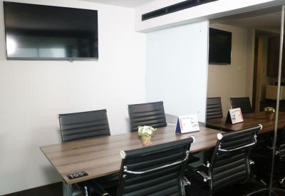 Compact meeting room with a wooden table, four black leather chairs, and a large wall-mounted monitor.