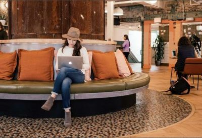 Coworking lounge with a curved green velvet bench and large orange cushions.