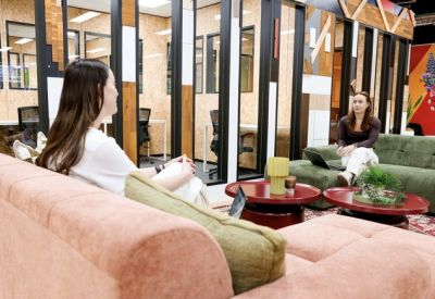 Bright lounge area with plush sofas and glass-walled private office pods in the background.