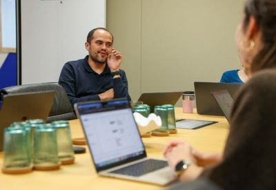 Sunlit meeting room with green glasses on the table and a man in a navy shirt.