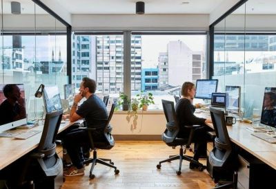 Open-plan workspace with glass partitions and desks facing large windows with city views.