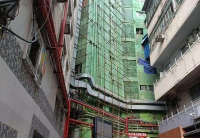 Narrow street view of building exterior with green facade and red industrial piping.