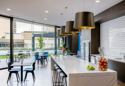 Bright communal kitchen and breakout area with marble island bench and hanging pendant lights.