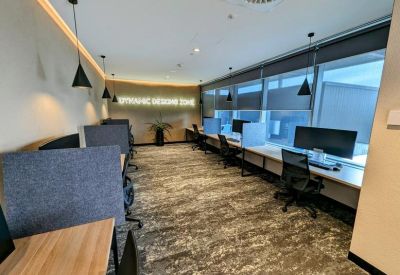 Modern coworking area featuring shared desks, privacy screens, and large windows with natural light.