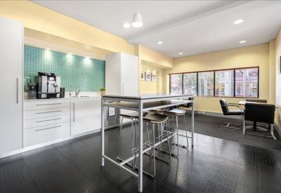 Modern communal kitchen and breakout area with a high breakfast bar and teal tiled backsplash.