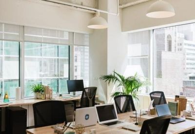 Bright open-plan workspace with multiple desks, ergonomic chairs, and large windows.