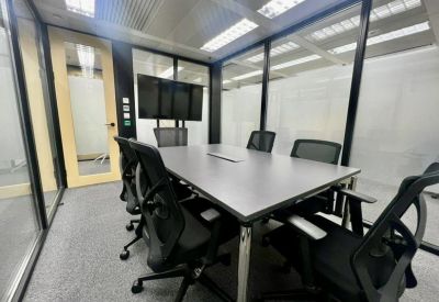 Modern glass-walled meeting room with a gray conference table and black ergonomic chairs.