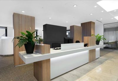 Modern reception desk with white and wood finishes and vibrant green potted plants.