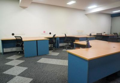 Open-plan office with multiple blue desks and black ergonomic chairs.