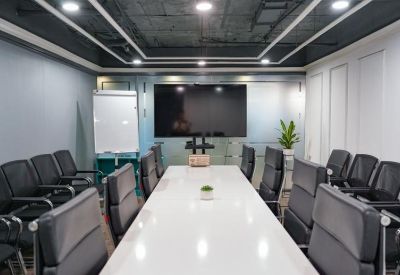 Professional meeting room featuring a long white table, black executive chairs, and a wall-mounted screen.