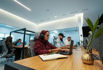 Employees working at long wooden desks in a bright, open-plan office.