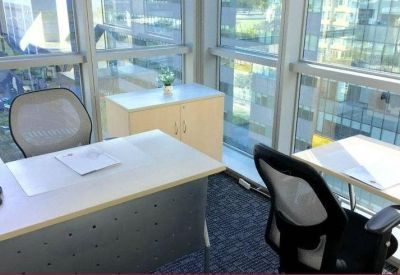 Bright corner office with two white desks and views of the city through floor-to-ceiling windows.