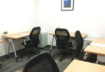 Internal office suite containing multiple wooden desks, black mesh chairs, and a framed wall print.