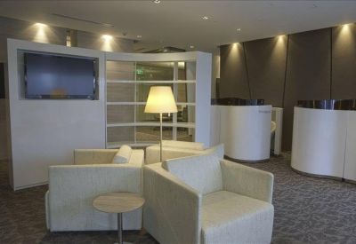 Modern lounge area with white armchairs, a curved privacy wall, and a TV.