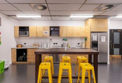 Modern office kitchen with light wood cabinetry and a high table with vibrant yellow stools.