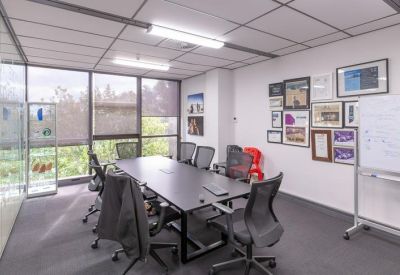 Professional meeting room with a large black table, mesh chairs, and a mobile whiteboard.