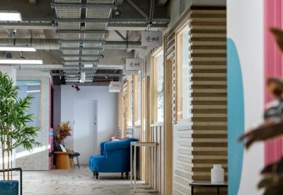 Modern industrial hallway with exposed ceiling pipes, plants, and a blue lounge chair.
