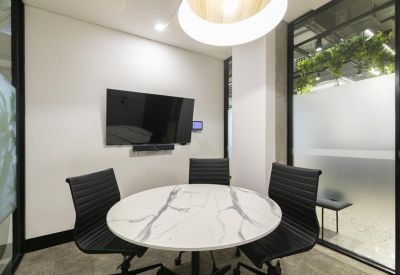 Compact meeting room with a marble-patterned round table and wall-mounted screen.