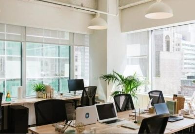 Bright open-plan office featuring wooden desks and large windows with city views.