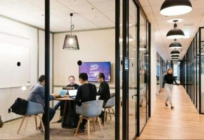 Modern glass-walled meeting room with people collaborating around a table.