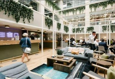 Spacious communal lounge with plants, sofas, and a service counter.