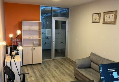 Private office with a vibrant orange feature wall, wooden flooring, and a grey sofa.