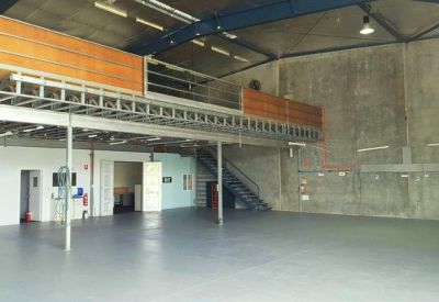 Spacious empty warehouse interior with a mezzanine level and high ceilings.
