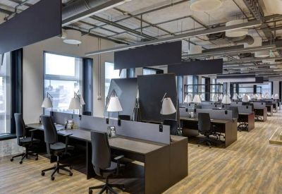 Industrial-style coworking space featuring dark desks, black chairs, and exposed ceiling pipes.
