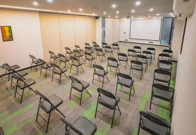 Spacious training or seminar room with rows of grey folding chairs and a projector screen.