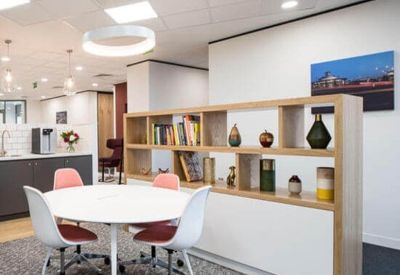 Communal breakout area with a round white table, pink chairs, and a wooden display shelf.