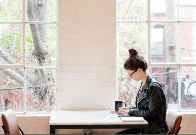 Bright office space with a person working at a white desk against large grid windows.