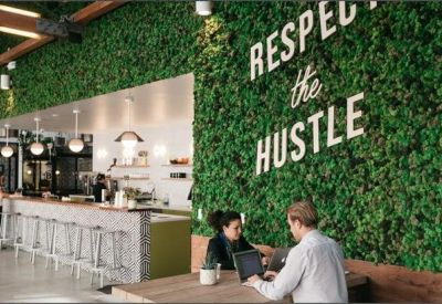 Breakout area featuring a lush green living wall with the text Respect the Hustle and cafe-style seating.