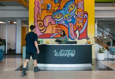 Reception desk featuring a bold neon logo and a large, colourful artistic mural background.
