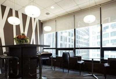 Communal breakout space with high tables, pendant lights, and floor-to-ceiling city views.