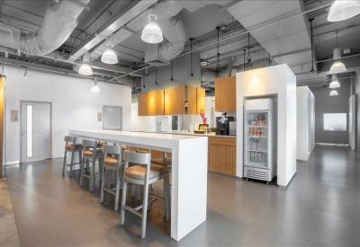 Modern communal kitchen area with a white breakfast bar, high stools, and a glass-door refrigerator.