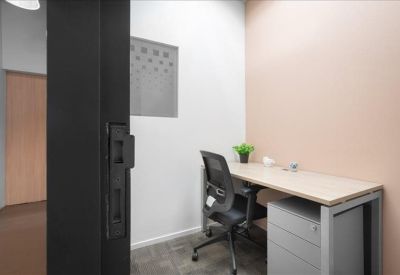 Compact private office with a light wood desk, ergonomic chair, and a small potted plant.