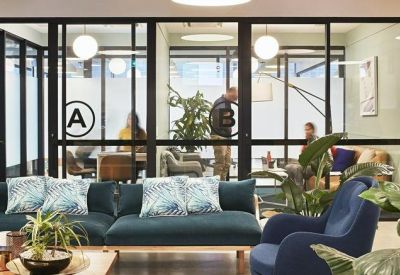 Modern coworking space featuring a dark teal sofa with patterned cushions and glass-partitioned offices.