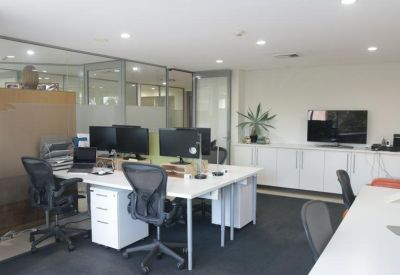 Wide-angle view of a bright workspace with multiple desks and a wall-mounted TV.