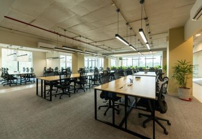 Open-plan office with wooden desks, ergonomic chairs, and industrial-style pendant lighting.
