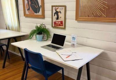 Modern white desk with a laptop, notebook, and framed art on the wall.