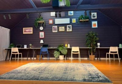Long communal desk with white and blue chairs under a dark purple feature wall.