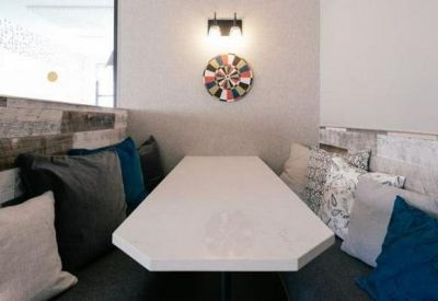 Communal breakout booth with plush grey and teal cushions and a white wood-panelled wall.
