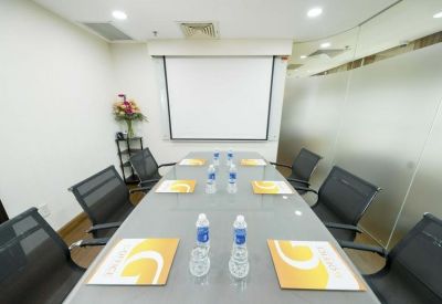 Meeting room with a long glass table, black chairs, and a projection screen.