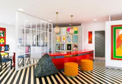 Vibrant coworking lounge with a red reception desk, orange ottomans, and bold striped flooring.