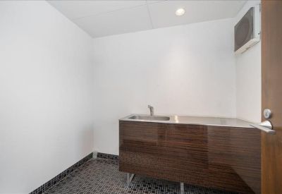 Minimalist communal kitchenette featuring a dark wood grain vanity and stainless steel sink.