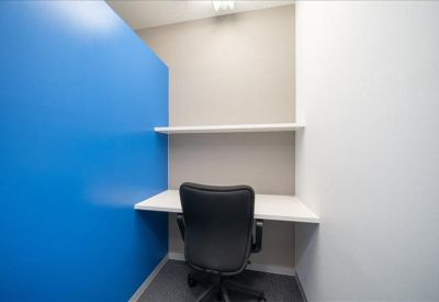 Private work booth with a bright blue accent wall and overhead shelving.