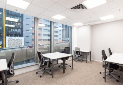 Bright corner office with desks and floor-to-ceiling windows showing city views.