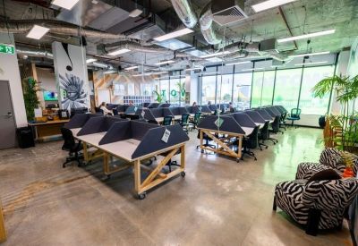 Spacious open-plan coworking area with rows of modern desks and large windows.