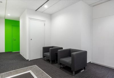 Small waiting area with two dark grey armchairs against a white and green wall.